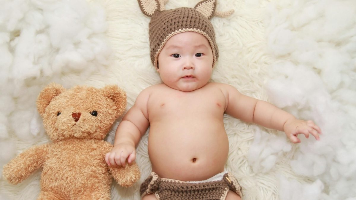 Cute baby posing with a teddy bear in a knitted outfit, exuding charm and innocence. Pediatric circumcision in calabasas