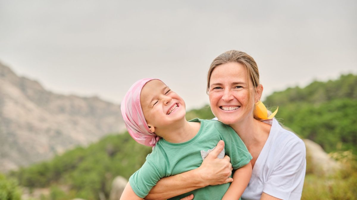 childhood tumors | Child with pediatric tumors, and mother smiling outdoors together